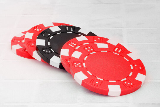 Shallow depth of field image of five poker chips, four red and one black, focus on black chip, shot on white background, chips laying on top of each other, space for text