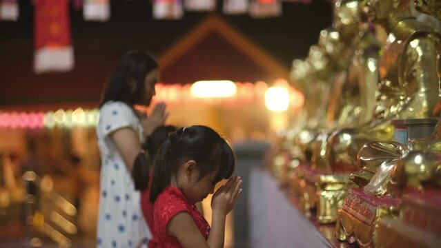 Happy Asian family, mother and children paying homage Buddha in temple to make a wish on the traditional Loy Krathong or Songkran festival in Thailand.
