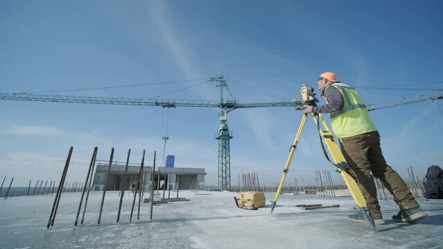 Geodetic works. Surveyor engineer in protective wear and red helmet using geodetic equipment at construction site. Professional equipment.