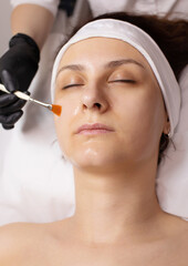 Closeup of a beauty therapist applying a face mask to a woman with perfect fresh skin. Cosmetology and facial skin care.