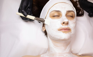 Close-up portrait of beautiful girl applying facial mask at cosmetology cabinet. 