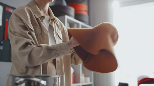 Selective focus of female hat-maker putting orange felt hat on stockpot with steam