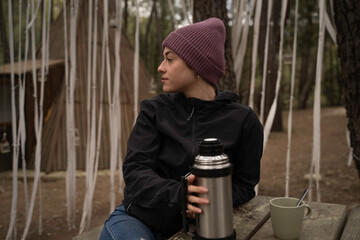 outside a Glamping , The smiling girl uses the thermos of coffee on a wooden table outdoors during...