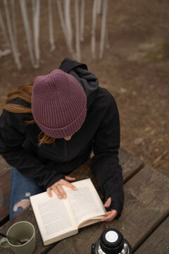 outside a Glamping , zenithal shot Smiling girl drinks coffee while reading a book on a wooden table outdoors during autumn.