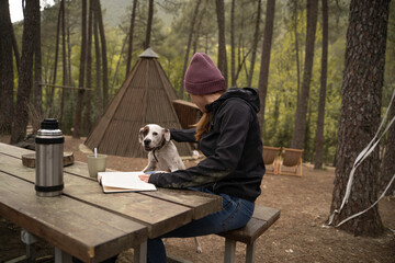 Outside a Glamping , The girl is with her dog and drinks coffee while reading a book on a wooden...