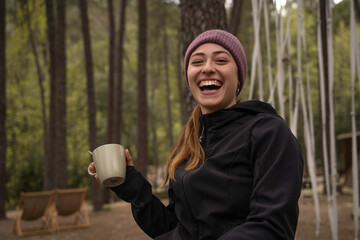 Outside a Glamping , The smiling girl holds a cup of coffee outdoors during the fall.