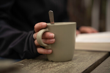 Glamping exterior, close-up detail of a woman's hands holding a cup of coffee while reading a book.
