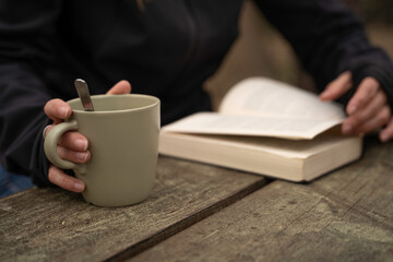 Glamping exterior, close-up detail of a woman's hands holding a cup of coffee while reading a book.