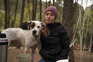 Girl wearing winter hat is sitting and petting her dog are outdoors