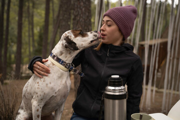 Girl wearing winter hat is sitting and petting her dog are outdoors