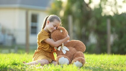 Happy teenage girl hugging her teddy bear friend outdoors on green grass lawn. Friendship concept