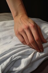 A close-up shot of a person's hand resting on a white sheet on a bed. 