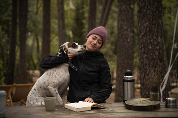 Chica con sombrero de invierno está sentado y acariciando a su perro están al aire libre