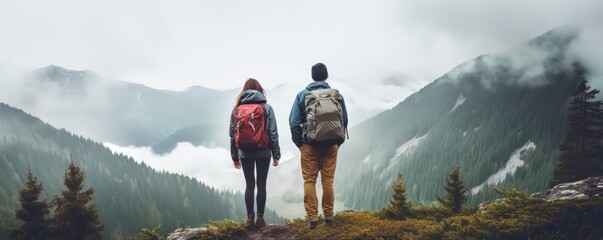 Enjoy nature away from city noise. A hikers couple stand with their backs to the camera against a foggy mountain landscape. Digital detox concept. - obrazy, fototapety, plakaty