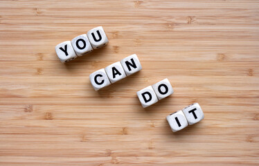 Word dice spelling the motivational mantra 'You can Do It' set on a pale orange bamboo background.