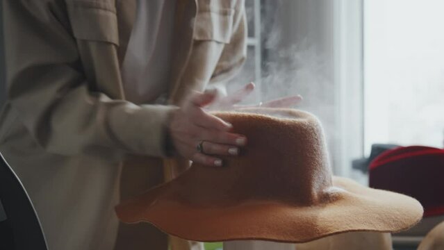 Selective focus of unrecognizable female hatter making new hat using steam from stockpot and special wooden mannequin