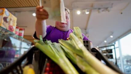 View from the cart side: A happy overweight man wearing a purple T-shirt walks through the supermarket, looks at the products. Shallots are already in the man's cart