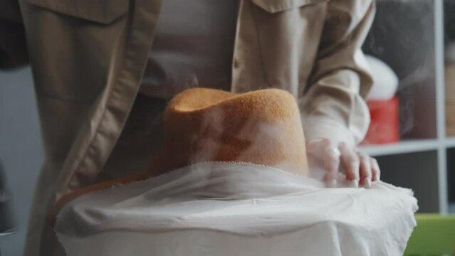 Close-up shot of unrecognizable Caucasian female artisan ironing new felt hat through cheesecloth
