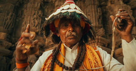 Authentic Portrait of an Old Indian Man in Traditional Attire Playing Instruments and Chanting in an Ancient Hindu Temple. Festive Senior Male Keeping Tradition and Cultural Heritage Alive - obrazy, fototapety, plakaty