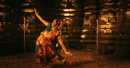 Portrait of an Expressive Young Indian Dancer Performing Folk Dance Choreography Inside an Ancient Temple. Woman in Traditional Clothes Dancing Bharatanatyam in a Colourful Sari