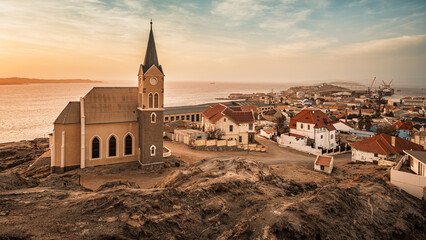 Panoramic view of Luderitz, Namibia, showcasing the Felsenkirche, the historic city Lutheran Church, and the German-style houses and buildings extending towards the port and the Atlantic Ocean. - obrazy, fototapety, plakaty