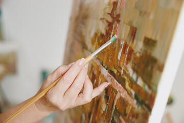 Close up cropped photo shot of female hold in hand arm brush paint artwork on easel with acrylic or...
