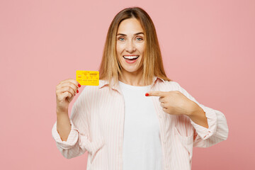 Young woman she wear shirt white t-shirt casual clothes hold in hand point index finger on mock up of credit bank card isolated on plain pastel light pink background studio portrait Lifestyle concept