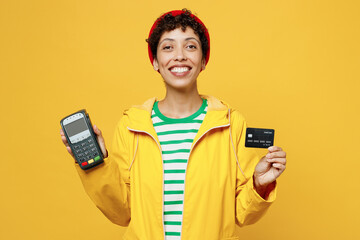 Young woman wears raincoat outerwear hat hold bank payment terminal process acquire credit card...