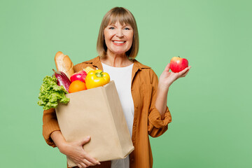Elderly smiling happy fun cheerful woman wearing brown shirt casual clothes holding in hand apple...