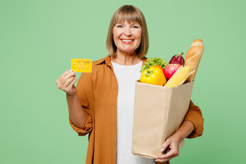 Elderly smiling happy rich woman wear brown shirt casual clothes hold mock up of credit bank card...