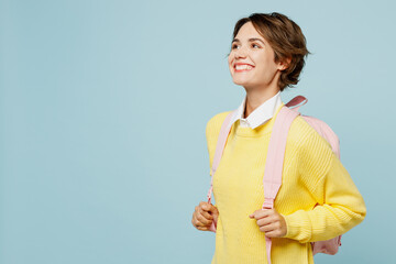 Side view young smiling minded happy cheerful woman student wearing casual clothes yellow sweater backpack bag looking aside isolated on plain blue background. High school university college concept.