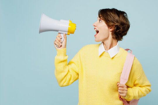 Young woman student wear casual clothes yellow sweater backpack bag hold megaphone scream announces discounts sale Hurry up isolated on plain blue background. High school university college concept.