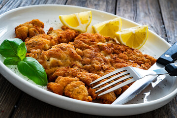 Crispy breaded seared chicken cutlet with lemon on wooden table
