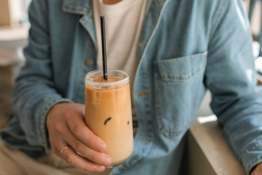 Close-up of a man sitting in a cafe holding a glass of iced coffee
