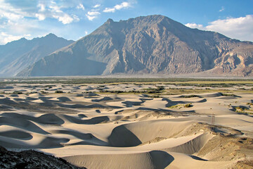 Sand dune pattern with mountain and blue clouds sky background in Nubra valley in Diskit, India.