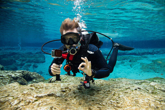 Underwater portrait of a scuba diver swimming near seabed making an ok sign, USA