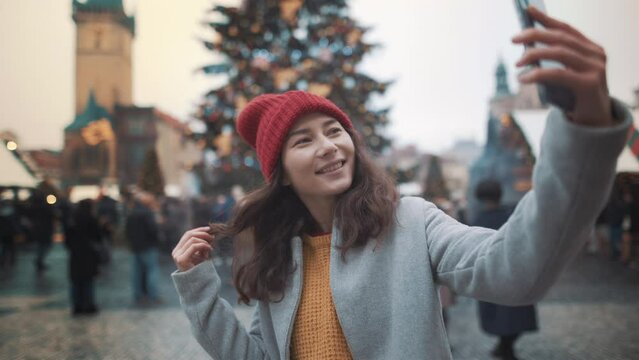 Young women portrait outdoor smile chat having a video call with friend or selfie at Christmas New Year holidays at illuminated background of decorated town square. Best friends enjoy winter vacation