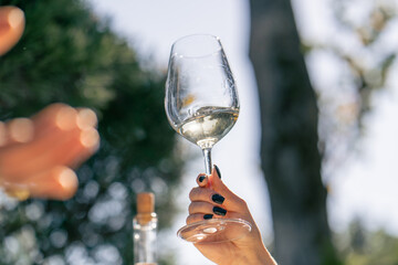Close-up shot of a woman's hand holding glass of wine by the stem and twisting it in the sun
