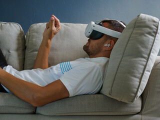 Man using virtual mixed reality glasses, wearing new generation vr headset for entertainment lying down on sofa.