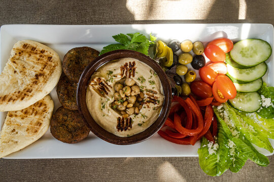 Overhead view of a meze platter with pita bread, hummus, falafel, olives, tomatoes, cucumber and lettuce