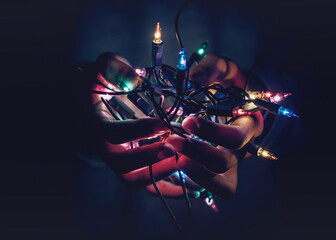 Close-up of hands cupped holding illuminated multi coloured Christmas string lights