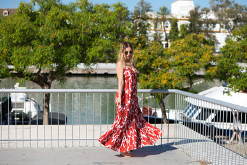 Blonde, young and beautiful woman with sunglasses and white dress with red print is having fun...