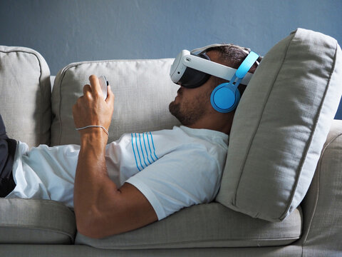 Man wearing new generation vr headset for entertainment lying down on sofa.