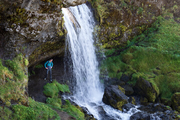 Fototapeta na wymiar Adult man standing behind Selvallafoss - the Sheep’s Waterfall in Iceland. Beautiful hidden waterfall in Snaefellsnes area