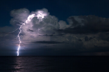 Naklejka na ściany i meble Bright lightning in the night over the ocean, concept of bad weather and bad weather.