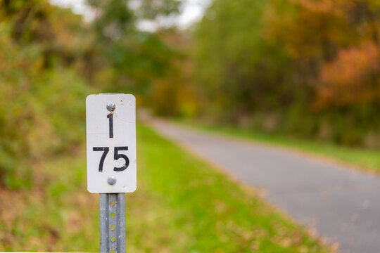 Fall, autumn, image of a mile marker sign, 1.75, along paved trail extending in the distance with orange leaves on the ground.	