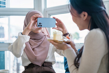 Happy asian Muslim blogger girl taking photos of her friend on a smartphone for social media.