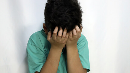 Sad child covering his face as a sign of depression, crying, anger. Child with shame. Boy angry and...