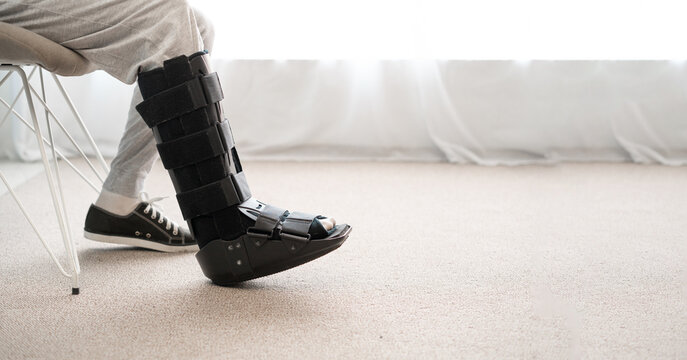 Injury man with black walker splint on leg sitting on the chair. Ankle foot orthosis