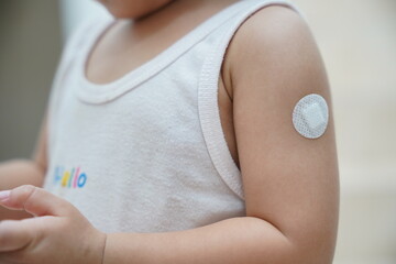 Little asian child girl with bandage plaster on her arm after vaccination. Close up of child girl arm after vaccination is completed. - obrazy, fototapety, plakaty